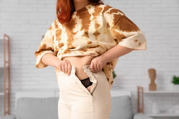 Image of woman trying to do her trousers up after pregnancy weight gain Airdrie