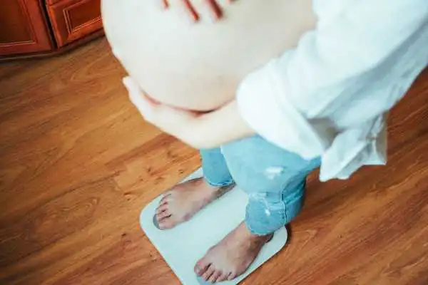 Image of woman weighing herself and experiencing weight gain through pregnancy Airdrie